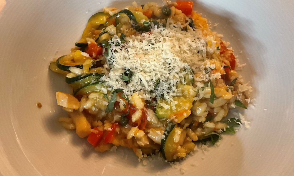 Risotto met kip, courgette, tomaat en paprika afgemaakt met fijngesneden oregano en parmezaanse kaas